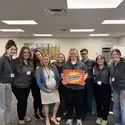 Nine people stand together while holding a sign that says Occupational Therapy
