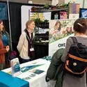 Students speak with attendees of a conference from behind a booth table.