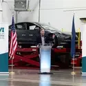 The College president speaks from a podium in front of a newly delivered Tesla electric vehicle.