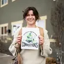 A smiling student holds a paper with a printed graphic.