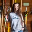 A student stands in a barn holding a pitchfork. 