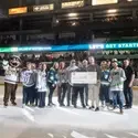 People pose for a photo holding a ceremonial check on the ice of a hockey game. 