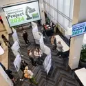 Students and members of the community browse research posters at an event. Screens display "Connections Project 2024."