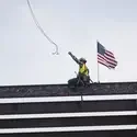 A construction worker throws off a wire attached to a crane that just lowered a beam onto a building's frame.