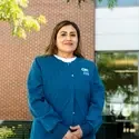 A student wearing nursing scrubs poses for a portrait in front of a brick building.