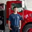 A firefighter poses for a photo in front of a firetruck.