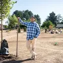 A man stands in a field with newly planted trees and employees working behind him.