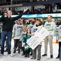 People stand on the ice as a man with a microphone address the audience at a hockey game.