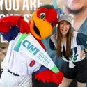 A woman wearing a College of Western Idaho baseball jersey smiles as she poses next to the Idaho Hawks mascot.