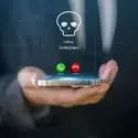 A photo of a hand holding a cellphone with a graphic of a skull, indicating a cyberscam.