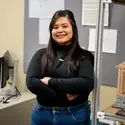 Student stands in front of billboard and next to shelving