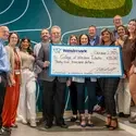 A group of people stand on a staircase smiling and holding a large ceremonial check