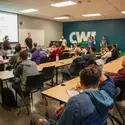 Students at desks with presenter in front of projection screen