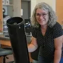 Stephanie Sevigny posing next to telescope in science lab