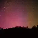 A photo of the night sky showing stars behind a silhouetted mountain top. 