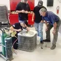 Students learn how to repair an air conditioning unit from an instructor.