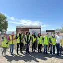 A group of volunteers pose at a park holding trash bags and rakes.