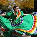 A dancer in traditional Hispanic dress dances at an outdoor event.
