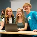 Three smiling students sit together in a classroom.