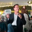 Person raising a bid paddle with the number 481 during an auction event, with string lights and attendees in the background.