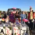A group of people stand around a decorated table set for a tea party with large playing cards and tea cups