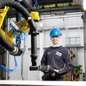 A mechatronics technician stands by a robotic machine in a manufacturing facility. 