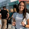 Student with a backpack on standing near a group of students and a bus