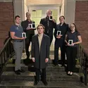 Six students stand on the steps in front of a building with awards