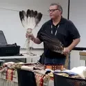 A Native American man demonstrates traditional ceremonial pieces in front of a class.