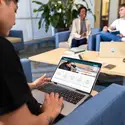 Individual looking up programs and degrees on a laptop in a common area around a few others