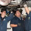 Three students working under a vehicle in the auto class.