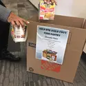 Individual placing canned food items in donation box. 