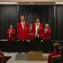 Five individuals in red blazers stand on a stage during an award ceremony.
