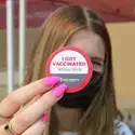 Woman holding up a sticker stating vaccination status