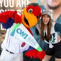 CWI student and mascot smile while holding a CWI pennant at a community event.