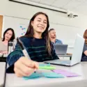 student in a classroom with other students writing on a sticky note
