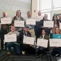 Faculty, staff, and students pose for a group portrait holding white signs with titles on them.