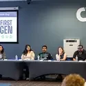 People sit at a table listening to a speaker talk about first-generation college students.