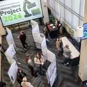 A photo of a student exhibit featuring project posters that line aisle partitions, taken from an elevated platform.