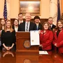 A group of students stand behind the Governor of the State of Idaho as he holds a proclamation. 
