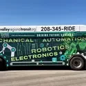 A city bus is parked and covered in a vinyl wrap featuring students and graphics.