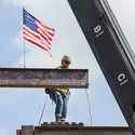 A construction worker standing on a steel beam gets ready to place a new beam, covered with signatures, onto a structure.