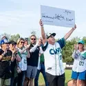 A young man holds up a ceremonial check on the field of a baseball game.