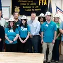 A group of students stand with government leaders wearing mining hats.