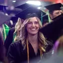 A graduated student wearing cap and gown smiles after receiving her diploma.