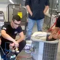 A group of students learn how to repair an air conditioning unit from an instructor.