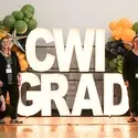 Staff posing in front of a CWI grad light and balloons sign at commencement