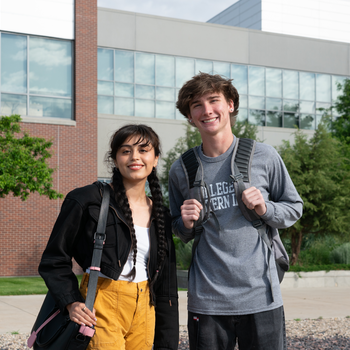 Two students with bags standing outside building