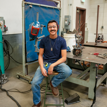 Person sitting on a stool, next to desk and welding tools