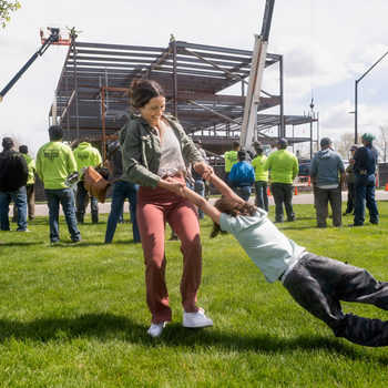 A woman smiles as she spins her son, celebrating in front of a new building being constructed in the background.